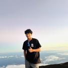 Smiling young man in black shirt holding a water bottle on a mountaintop above clouds