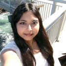 Woman taking selfie on sunny waterfront bridge, long dark hair, white top